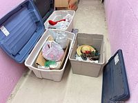 Three open plastic totes showing bags of ornaments, red stocking, straw wreath with pinecones