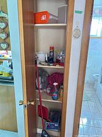 Closet shelves with broom, dustpans, tableware and cleaners visible