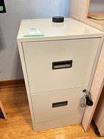 Front view of beige metal 2-drawer filing cabinet showing recessed handles and keyed lock with keys