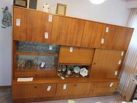 Front view of full teak wall unit showing upper cabinets, glass display section, drop-front bar, lower drawers