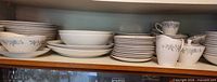 Cabinet shelf showing stacks of dinner plates, salad plates, bowls, saucers, teacups, creamer and sugar bowl