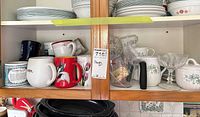 Cabinet shelf with Corelle plates and bowls, assorted mugs, glass dessert coupes, creamer, measuring cup