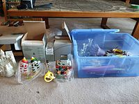 overview of lot showing ceramic white church luminary, boxed items, two snowman figurines, chimney house luminary and tote with additional items