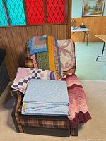 Multiple folded quilts and afghans on chair