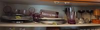 Shelf view showing purple tumblers, glass cake stand, plates, silver goblets, glass condiment set