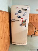 Front view of refrigerator showing cream finish, logos, chrome handle and general wear