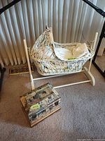 Overall lot showing wicker bassinet on stand with linens inside and wooden keepsake box beside
