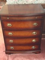 Front view showing four drawers, curved front, brass-tone pulls, shaped feet
