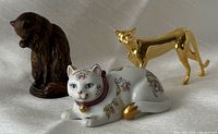 Group view of three miniature cat figurines on fabric backdrop