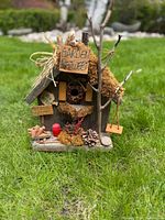 Front view showing moss roof, twig branch, swing, signs, watering can, wagon, pinecone