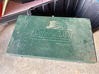 Closed green metal Coleman stove showing embossed logo on lid
