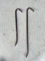 Two rusted steel crowbars laid on concrete, showing both hooked and chisel ends