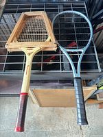 Both tennis rackets displayed on a table, vintage wooden racket in press on left, modern composite racket on right