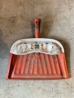 Front of red dustpan showing decorative white rim and handle