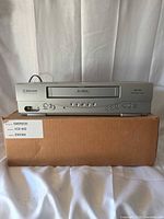 Front view of silver Emerson EWV404 VCR on box