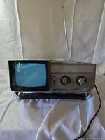 Front view of JCPenney 5-inch micro television with screen illuminated, antenna extended, AC cord visible