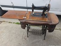 Full view of Paragon sewing machine installed in oak treadle cabinet with extension leaf open