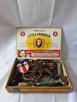 Open cigar box displaying knives, cords, badge and other small items