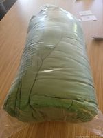 Rolled green sleeping bag sealed in plastic on tabletop