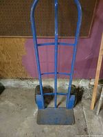 Full view of blue steel hand truck standing upright on floor