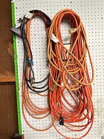 Two bundles of orange and black heavy-duty cords hanging on pegboard