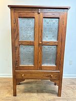 Front view of closed oak pie safe showing tin panels and drawer