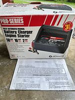 Front of retail box displaying model, output specs, clamps shown, manual in foreground