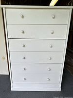 Front view of white chest showing six drawers with knobs