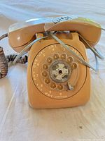 Front view of beige rotary telephone showing dial and attached cords
