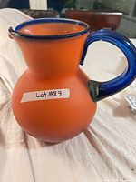 Full view of orange frosted glass pitcher with blue handle