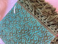 Folded bedspread showing turquoise and olive woven floral pattern and fringe