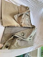 Two folded curtains with metal grommets, beige and grey