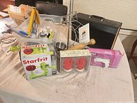 Group shot showing boxed apple peeler, lobster shakers, vinyl gloves, wire stand, wooden rolling pin, plastic tub and contents