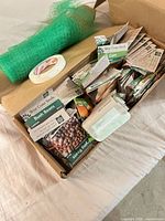 Box with seed packets, green netting roll and tape roll visible