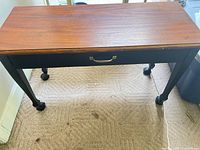 Top view of table showing brown wooden surface, black base, brass-tone handle, casters
