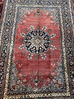 Full view of rug showing red field, floral medallion and borders