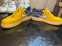 Side view of both sneakers showing yellow upper, white swoosh, blue heel panel, minor sole discoloration