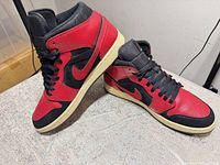 Oblique view of both shoes showing red leather uppers, black swoosh and laces