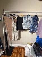 Rack with five garments: beige pants, floral dress, black blouse, two denim vests