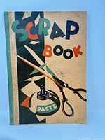 Front cover of scrapbook showing title graphics, scissors and paste illustration