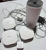 Group shot of three eero routers, one TP-Link Deco router, power adapters