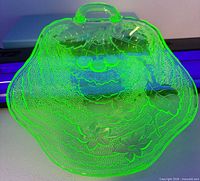 Platter glowing bright green under UV light showing embossed details and handle