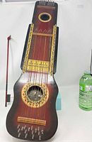 Front view of red sunburst Ukelin showing strings, decorative stenciling, tuning pins