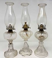 Front view of three pressed glass oil lamps with chimneys and burners