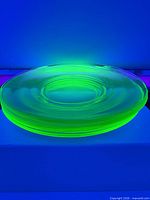 Stack of green uranium glass saucers glowing under UV light