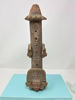 Front view showing entire terracotta ocarina with face mask, side figures, finger holes and flared top