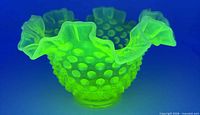 Dish glowing bright green under UV showing hobnail pattern and ruffled rim