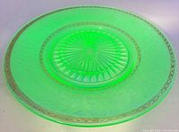 Full view of green etched glass dinner plate showing etched floral border, starburst center, and gold rim