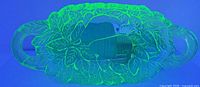 Serving bowl glowing bright green under UV light showing leaf and pear design