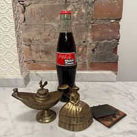 Group view of brass bell, Aladdin lamp, silver locket with Coke bottle for scale